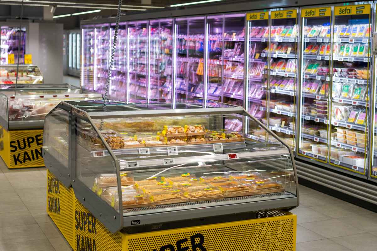 Parduotuvės šaldikliai pilni maisto produktų ir įrengta vitrina su desertais.